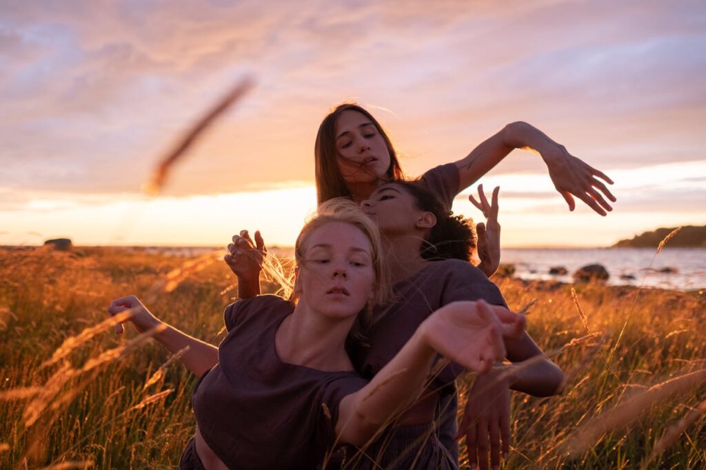 A group of women engaging in a graceful dance in a sunlit grass field during sunset.
