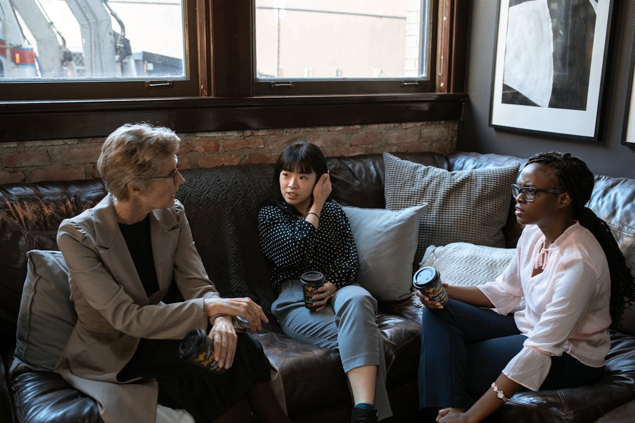 programs-03 Three diverse women enjoying a coffee break and engaging in conversation in a stylish office setting.